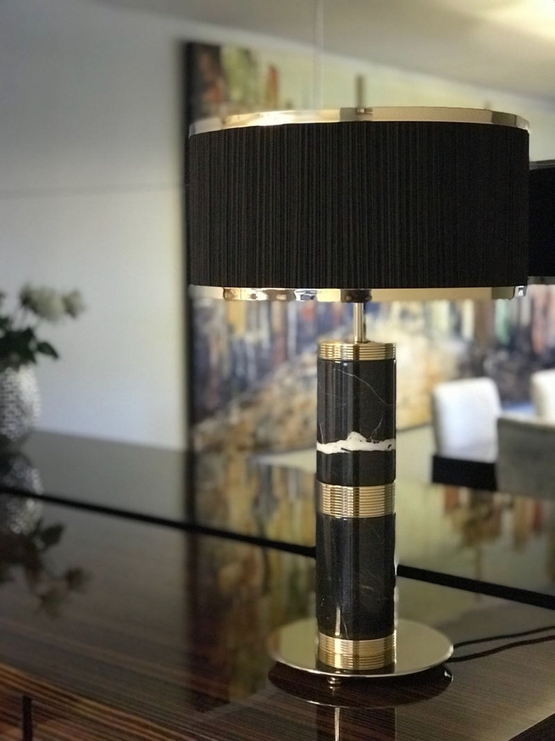 Close-up view of the Aurelian Light table lamp. Gold-plated brass rings adorn a smooth marble base, showcasing the exquisite craftsmanship of this luxury lighting piece.